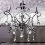 Silver chandelier with crystal ornaments hangs in an elegant party hall in Queens, NY, featuring a patterned ceiling.